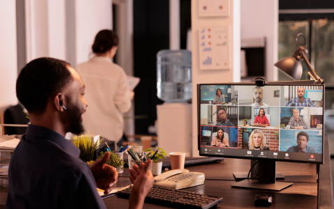 Man looking at a monitor during a virtual meeting with coworkers visible on the screen